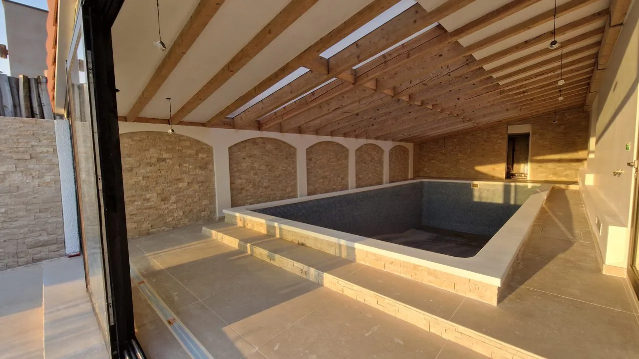 Piscine intérieure rénovée : bassin mosaïque, parement pierre et charpente bois