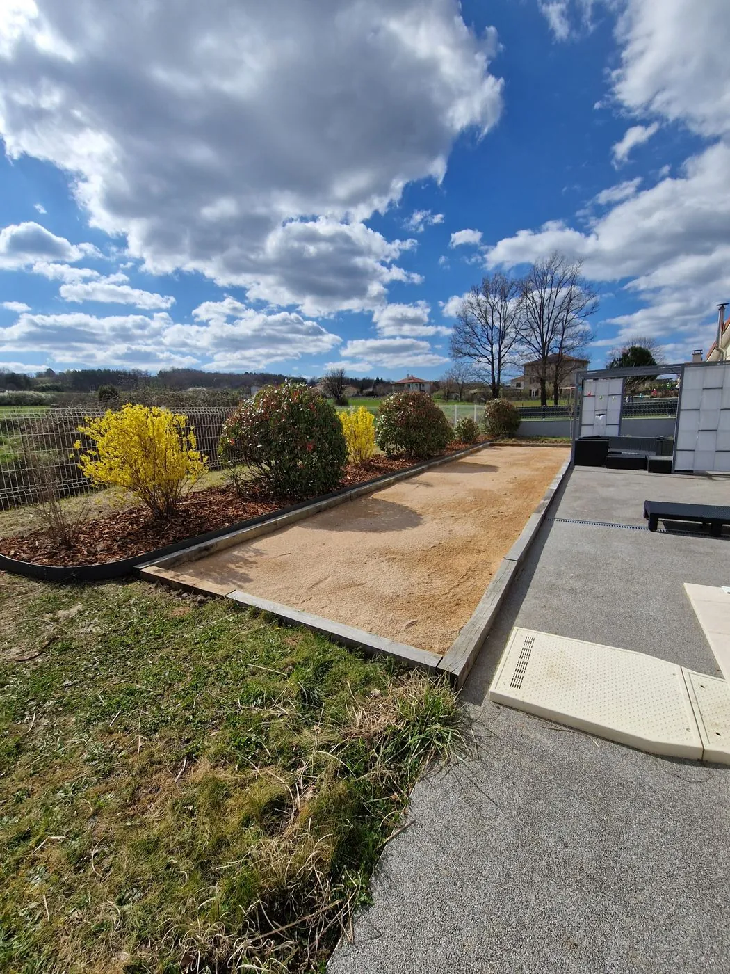 Terrain de pétanque aménagé et bordé de massifs.